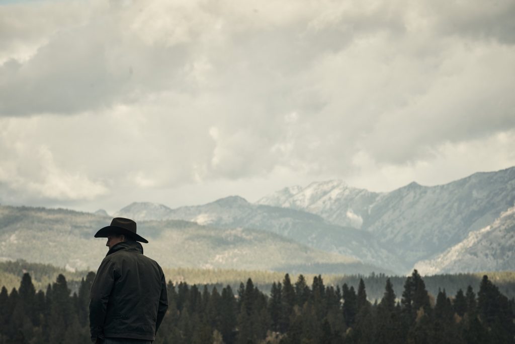 Yellowstone television show review. Kevin Costner, who plays John Dutton, looks out at a mountain range. yellowstone review