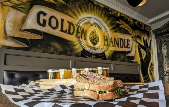Photo of a sandwich, flight of beers in front of the Golden Handle logo in Spokane, WA