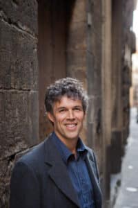 Photo of author Tom Mueller in an alley in Italy wearing professional clothing