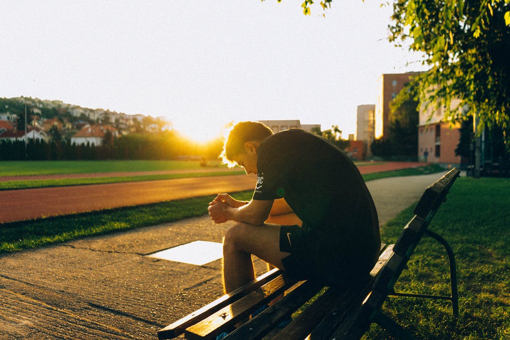 Man Sitting on Bench Near Track Field While Sun Is Setting
