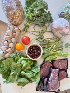 Vegetables laid out on the counter including lettuces, garlic scapes, tomatoes and more and meats like chicken and beef. Linc Box Review