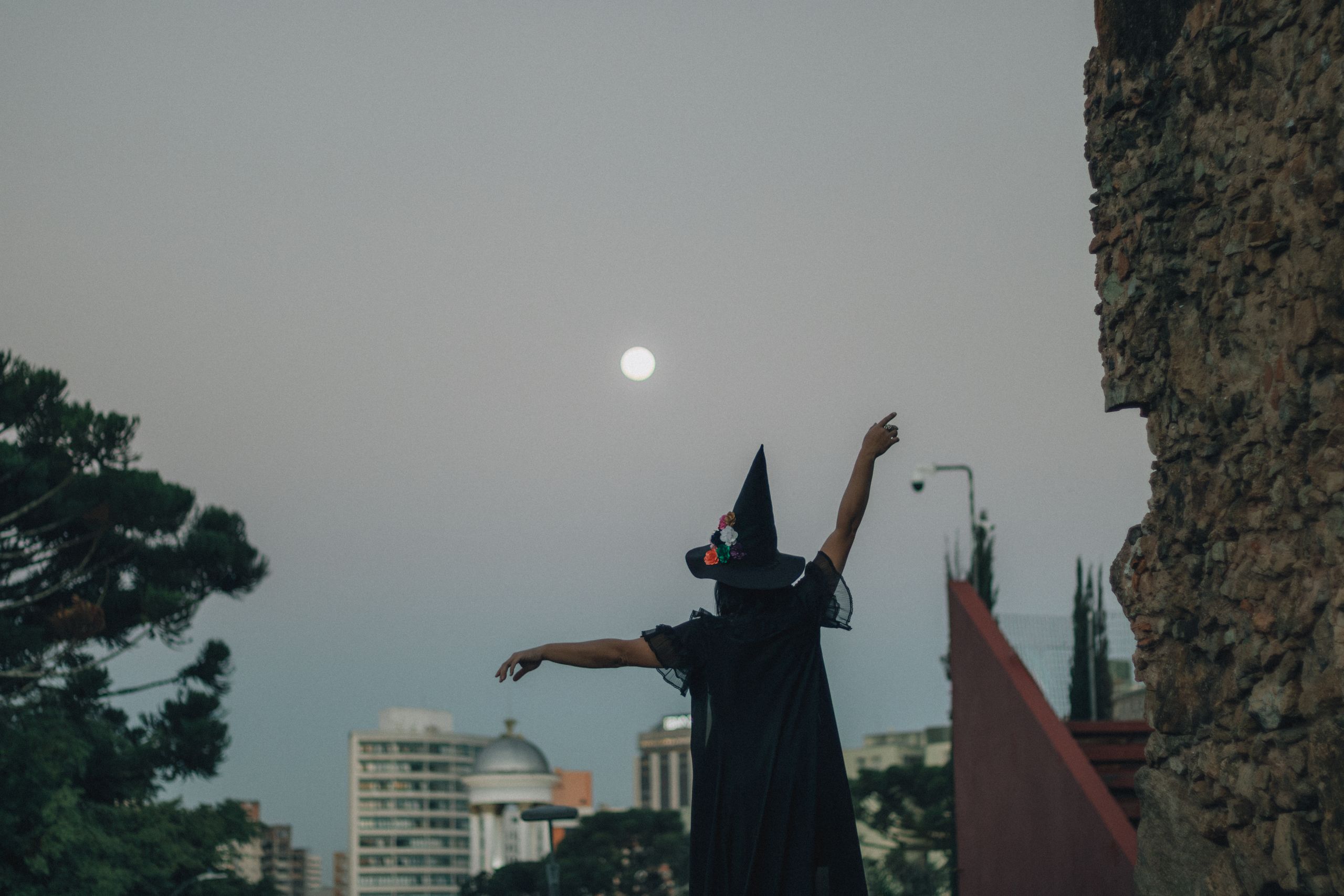 Silhouetted witch casting spell under full moon in cityscape, mysterious ambiance.